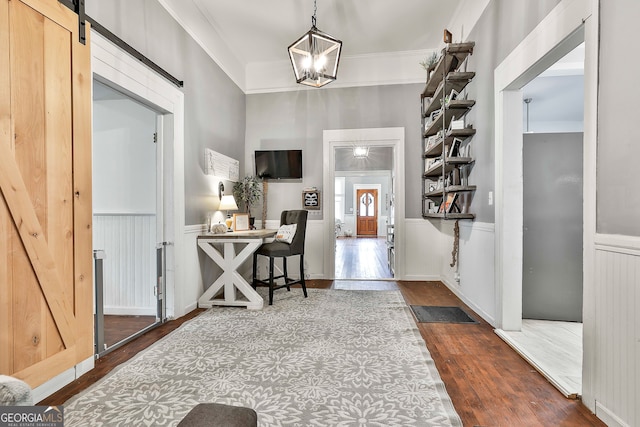 foyer featuring ornamental molding, an inviting chandelier, a barn door, and dark hardwood / wood-style flooring