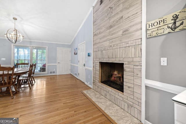 living room with light wood-type flooring, vaulted ceiling, an inviting chandelier, and ornamental molding