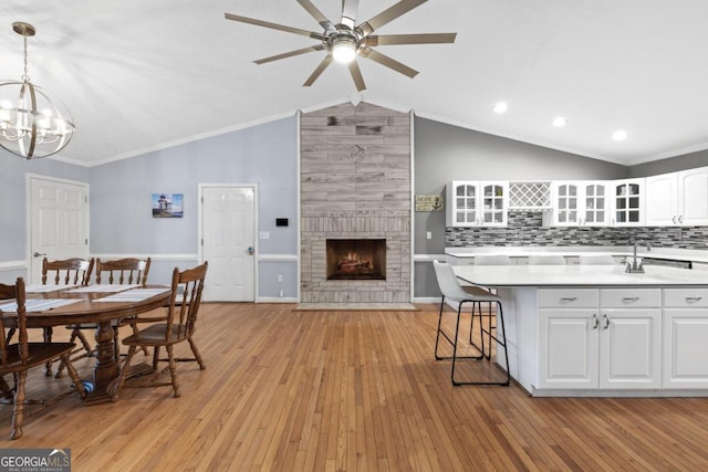 dining space featuring a large fireplace, ornamental molding, lofted ceiling, and light wood-type flooring