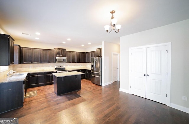 kitchen featuring appliances with stainless steel finishes, dark wood-type flooring, an inviting chandelier, a center island, and decorative light fixtures