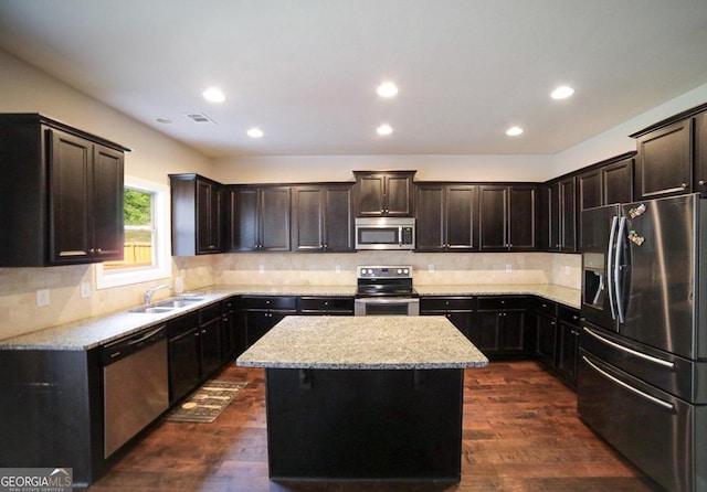 kitchen featuring light stone countertops, dark hardwood / wood-style flooring, stainless steel appliances, a center island, and sink