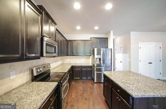 kitchen with stainless steel appliances, dark hardwood / wood-style floors, a center island, light stone countertops, and decorative backsplash