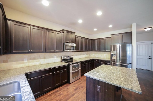 kitchen featuring a kitchen island, dark brown cabinets, dark wood-type flooring, stainless steel appliances, and light stone countertops