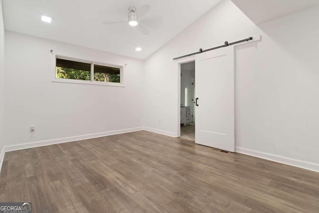 empty room with ceiling fan, hardwood / wood-style flooring, lofted ceiling, and a barn door