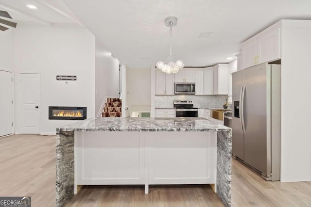 kitchen featuring stainless steel appliances, white cabinets, light wood-type flooring, and decorative light fixtures