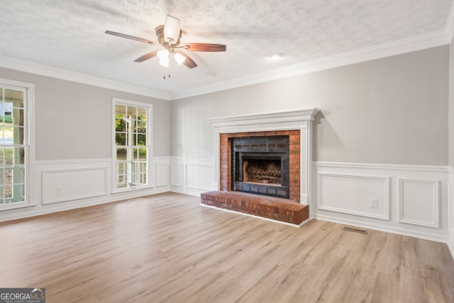 unfurnished living room featuring a brick fireplace, a textured ceiling, light hardwood / wood-style flooring, and ornamental molding