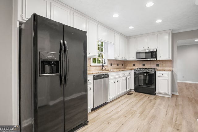 kitchen with light wood-type flooring, sink, white cabinetry, black appliances, and light stone countertops