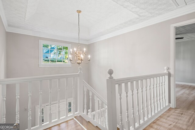 staircase featuring a raised ceiling, ornamental molding, a chandelier, and hardwood / wood-style flooring