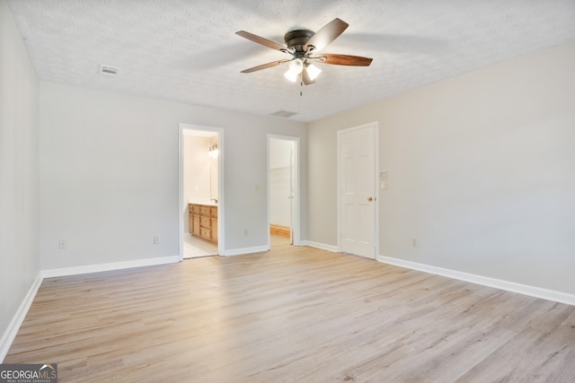 unfurnished bedroom with ceiling fan, a textured ceiling, ensuite bathroom, and light hardwood / wood-style floors