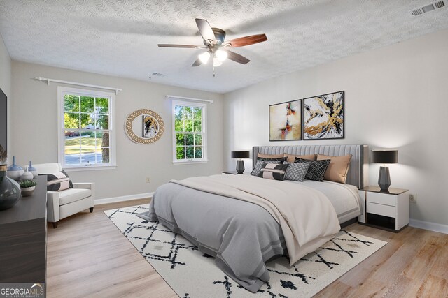 bedroom with light hardwood / wood-style floors, a textured ceiling, and ceiling fan