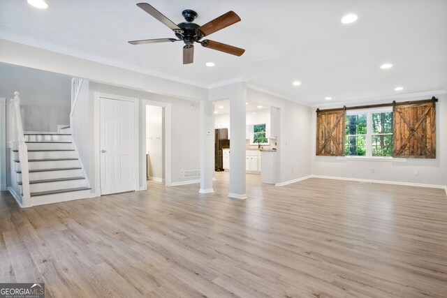 unfurnished living room featuring light wood-type flooring, crown molding, ceiling fan, and a barn door