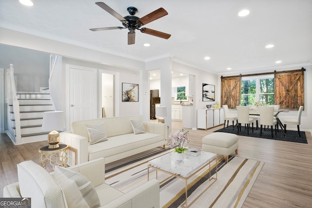 living room featuring ornamental molding, light wood-type flooring, ceiling fan, and a barn door