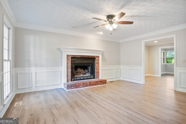 unfurnished living room featuring ceiling fan, light wood-type flooring, crown molding, and a brick fireplace