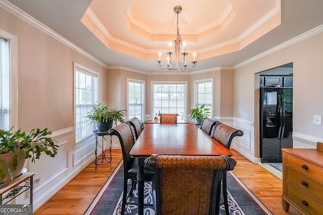 dining space with a notable chandelier, light wood-type flooring, crown molding, and a raised ceiling