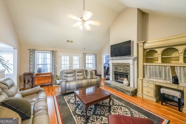 living room featuring high vaulted ceiling, ceiling fan, a stone fireplace, and light hardwood / wood-style flooring