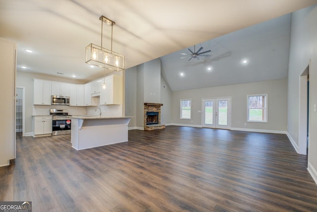 unfurnished living room featuring ceiling fan, dark wood-type flooring, sink, high vaulted ceiling, and a stone fireplace