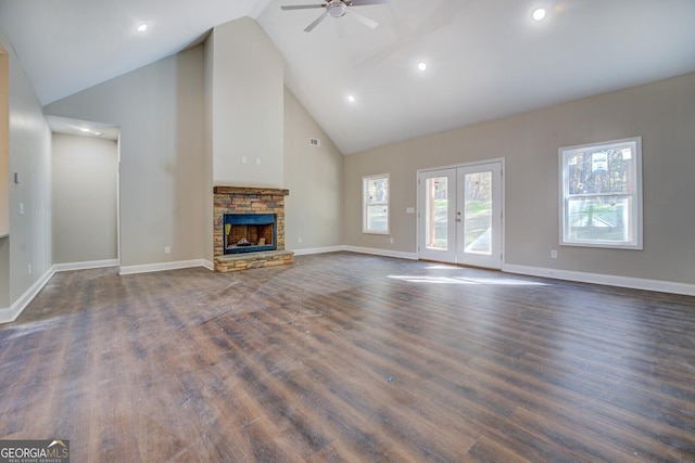 unfurnished living room with ceiling fan, french doors, a stone fireplace, high vaulted ceiling, and dark hardwood / wood-style floors