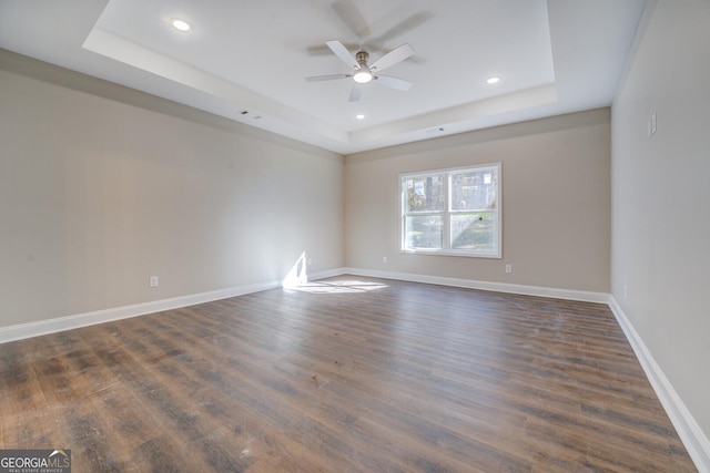 spare room with a raised ceiling, ceiling fan, and dark wood-type flooring