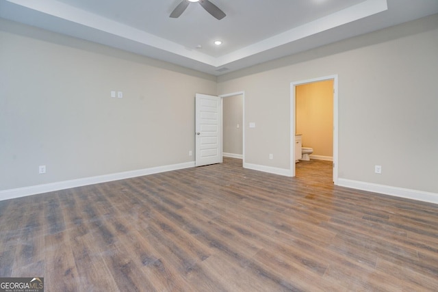 unfurnished bedroom featuring ceiling fan, dark hardwood / wood-style flooring, connected bathroom, and a tray ceiling