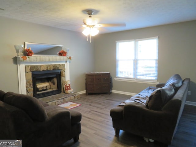 living room featuring a textured ceiling, a stone fireplace, hardwood / wood-style floors, and ceiling fan