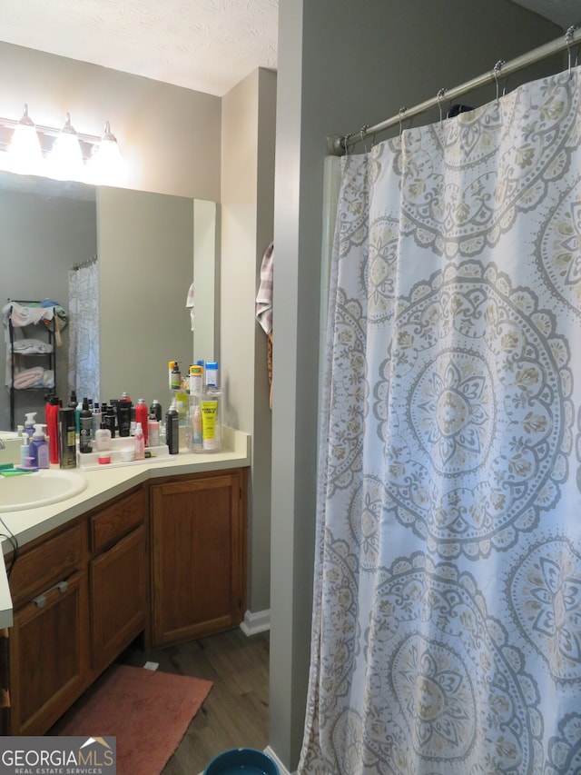 bathroom featuring wood-type flooring, vanity, walk in shower, and a textured ceiling