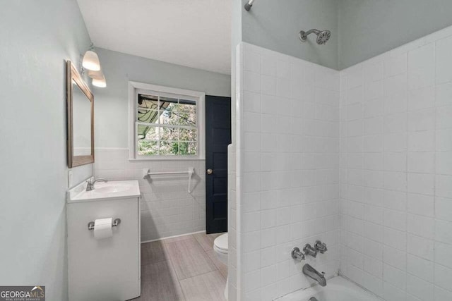 full bathroom featuring tile walls, vanity, toilet, and tiled shower / bath