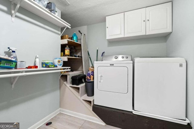 laundry area featuring cabinets, light wood-type flooring, a textured ceiling, and washing machine and clothes dryer