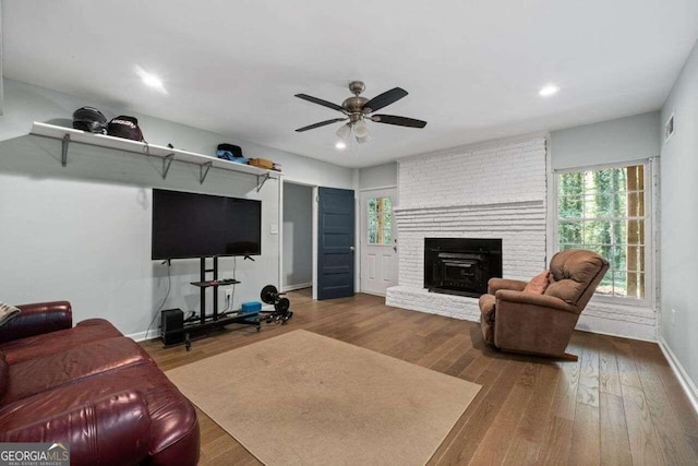 living room with wood-type flooring, a brick fireplace, and ceiling fan