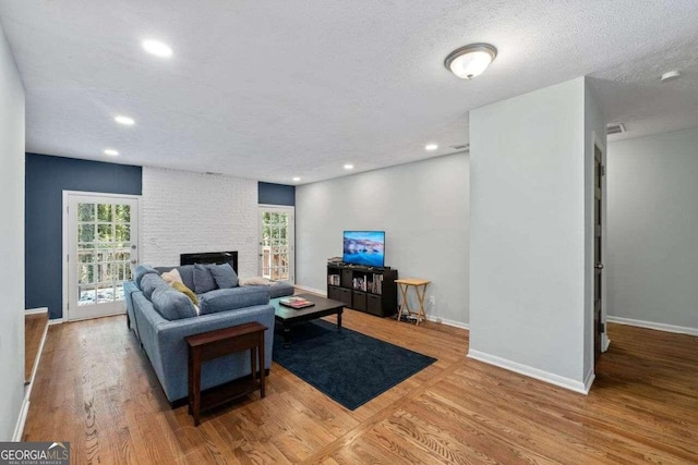 living room with light wood-type flooring, a textured ceiling, and a stone fireplace