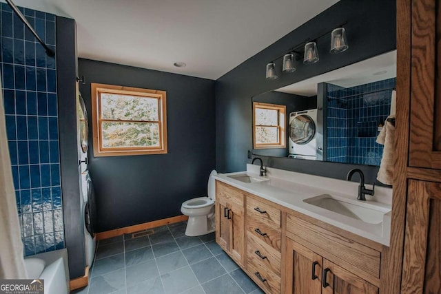 full bathroom with vanity, toilet, stacked washer and clothes dryer, shower / bath combo with shower curtain, and tile patterned flooring