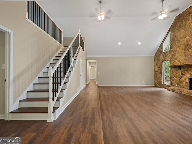 unfurnished living room with ceiling fan, ornamental molding, wood-type flooring, and a stone fireplace