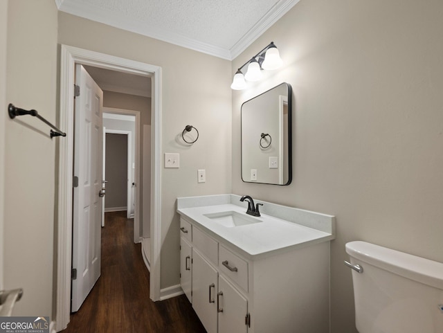 bathroom with a textured ceiling, wood-type flooring, vanity, toilet, and ornamental molding