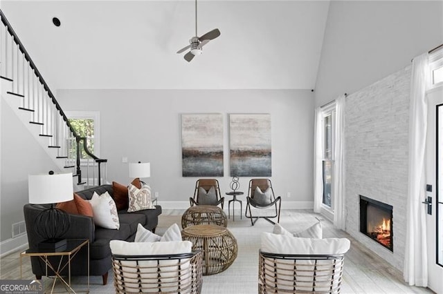 living room featuring ceiling fan, a stone fireplace, light wood-type flooring, and high vaulted ceiling