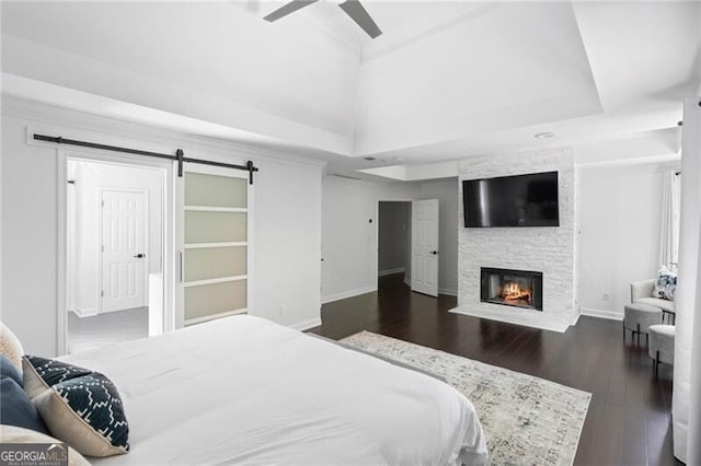 bedroom with ceiling fan, a fireplace, dark hardwood / wood-style floors, and a barn door