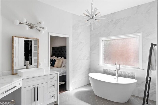 bathroom with vanity, a tub, tile patterned floors, an inviting chandelier, and tile walls