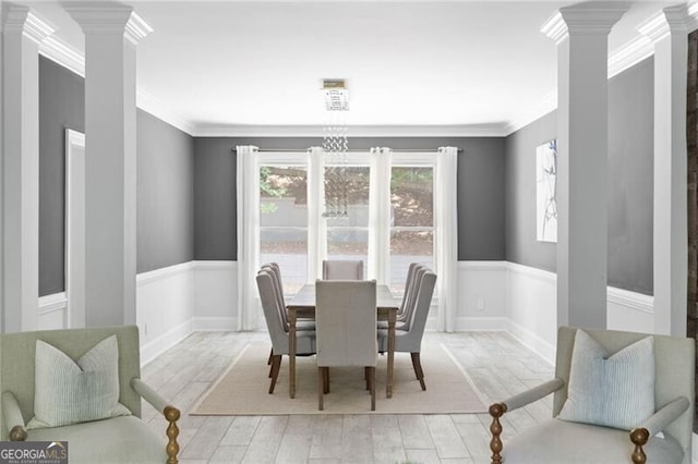 dining area featuring light wood-type flooring, crown molding, decorative columns, and a chandelier