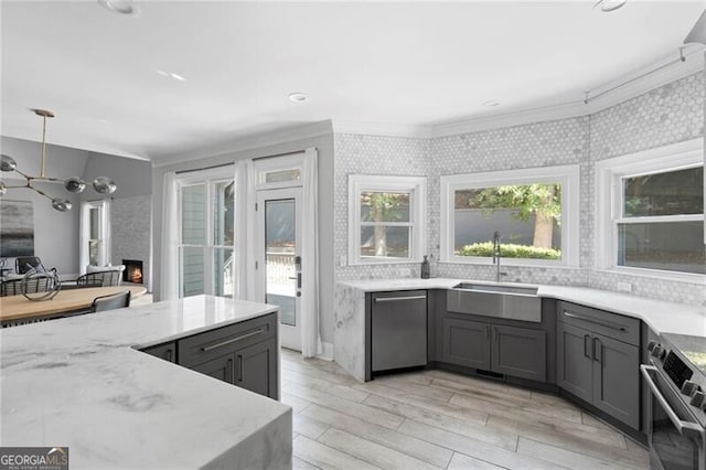 kitchen with gray cabinets, crown molding, light hardwood / wood-style flooring, a large fireplace, and appliances with stainless steel finishes