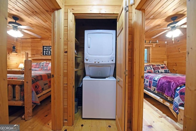 clothes washing area with ceiling fan, wooden walls, light hardwood / wood-style flooring, and stacked washer and dryer