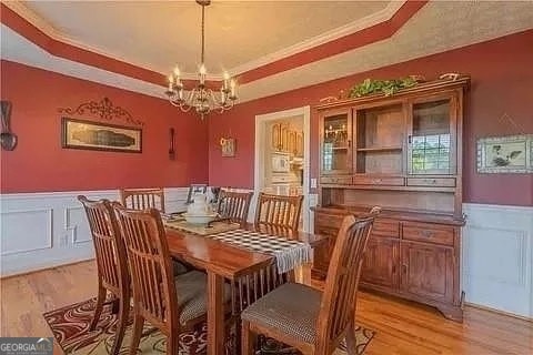 dining space featuring ornamental molding, a notable chandelier, a tray ceiling, and light wood-type flooring