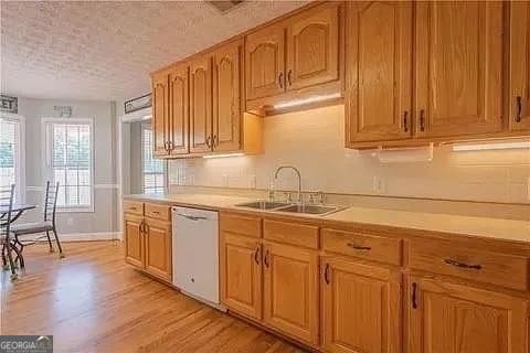 kitchen with light hardwood / wood-style floors, a textured ceiling, sink, and dishwasher