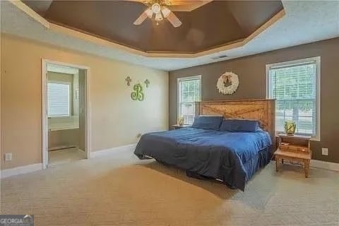 bedroom featuring ensuite bath, a raised ceiling, carpet floors, and ceiling fan