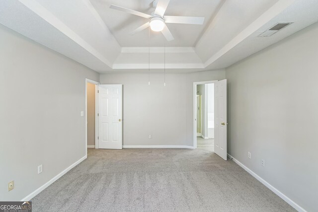 carpeted empty room featuring a tray ceiling, visible vents, baseboards, and ceiling fan