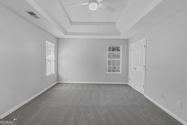 empty room featuring carpet floors, a ceiling fan, visible vents, and a raised ceiling