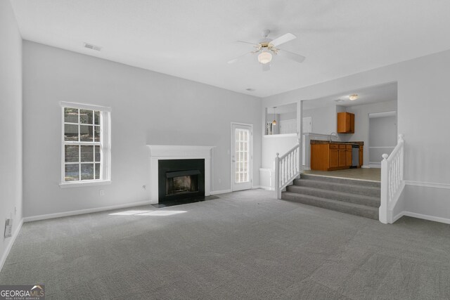 unfurnished living room featuring a fireplace with flush hearth, a sink, stairs, ceiling fan, and carpet floors