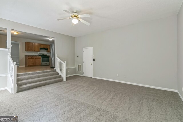 unfurnished living room with a ceiling fan, stairs, and carpet