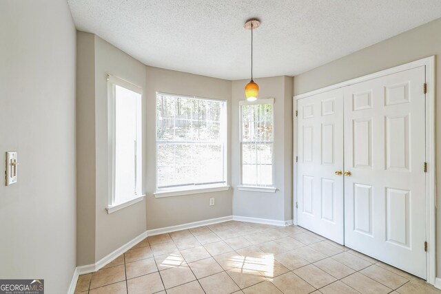 unfurnished dining area with light tile patterned floors, baseboards, a textured ceiling, and plenty of natural light