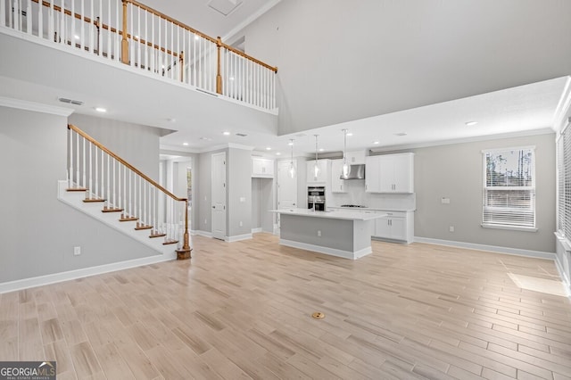 unfurnished living room featuring light wood-type flooring, ornamental molding, and a towering ceiling