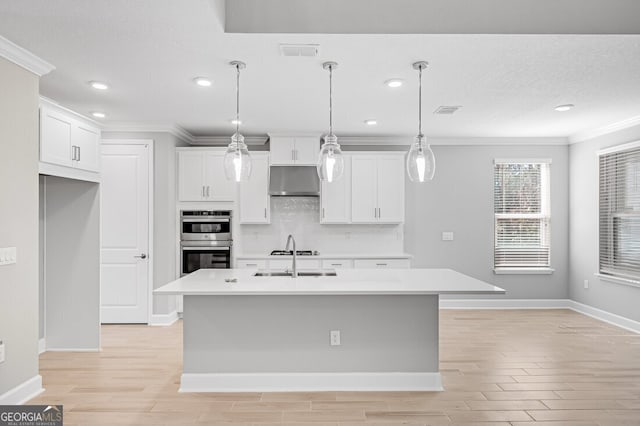 kitchen featuring a center island with sink, hanging light fixtures, double oven, crown molding, and white cabinetry