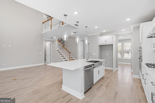 kitchen with an island with sink, white cabinetry, hanging light fixtures, stainless steel appliances, and sink