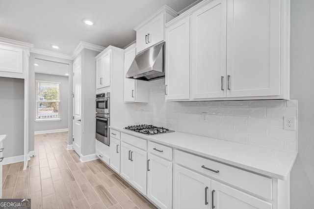 kitchen with appliances with stainless steel finishes, light hardwood / wood-style flooring, white cabinets, decorative backsplash, and ornamental molding